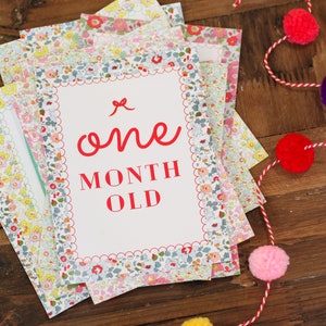 May include: A stack of white cards with a floral pattern border. The top card has a red border and says "one month old" in red text.