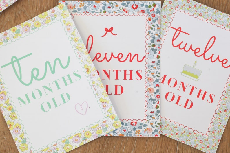 May include: Three white cards with floral borders and red text. The cards say "ten months old", "eleven months old", and "twelve months old".