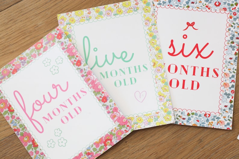May include: Three white cards with floral borders and pink, green, and red text. The cards say "four months old", "five months old", and "six months old".