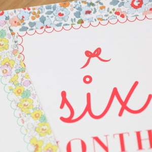May include: A white card with a red scalloped border and a red bow. The card says "six months" in red lettering.