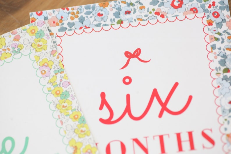 May include: A white card with a red scalloped border and a red bow. The card says "six months" in red lettering.