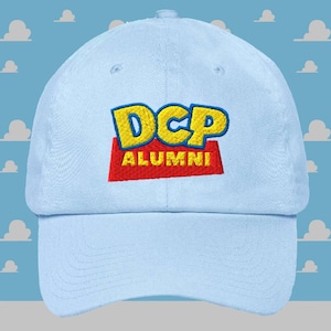 Peut inclure: Casquette de baseball bleu clair avec le texte brodé "DCP ALUMNI" en lettres jaunes et bleues sur un rectangle rouge. La casquette est en tissu doux et possède une visière incurvée.