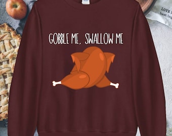 Può includere: Una felpa color granata con la scritta "Gobble Me, Swallow Me" e un'immagine di un tacchino arrosto in stile cartone animato.