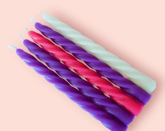 May include: A set of five long, slender, spiral-shaped taper candles arranged diagonally. The collection includes two purple candles, one bright pink candle, one deep violet candle, and one off-white candle, each featuring a small white wick.