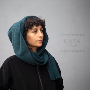 Könnte beinhalten: Ein teal-farbenes Kapuzen- und Schal-Set. Die Kapuze ist über Kopf und Schultern drapiert, der Schal um den Hals gewickelt. Die Person trägt eine schwarze Jacke. Der Text "KAYA WEAR" ist sichtbar.