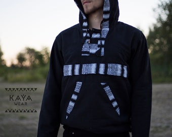Puede incluir: Una sudadera con capucha negra con patrones geométricos blancos. La sudadera tiene una capucha con cordón y un cierre de botón. El modelo lleva pantalones negros.