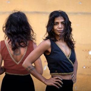 Puede incluir: Dos mujeres vistiendo tops de envoltura negros y color óxido con ribetes dorados. Los tops son sin mangas y tienen un escote en V. Las mujeres están de pie frente a una pared amarilla. El texto "KAYA WEAR" es visible en la esquina inferior derecha de la imagen.