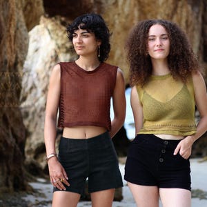 May include: Two women wearing sleeveless tops and shorts. The woman on the left is wearing a brown top and black shorts. The woman on the right is wearing a yellow top and black shorts.