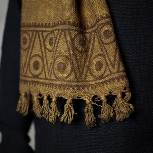 May include: A brown scarf with a geometric pattern of circles and triangles. The scarf has a fringe on the bottom.