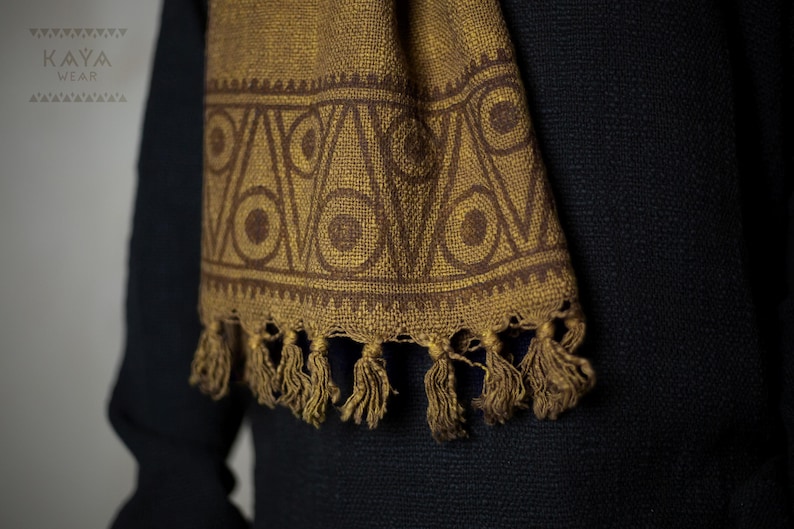 May include: A brown scarf with a geometric pattern of circles and triangles. The scarf has a fringe on the bottom.