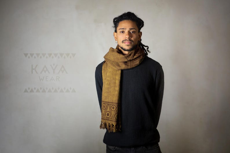 May include: A person wearing a black long-sleeved shirt with a brown patterned scarf. The scarf has a geometric design and is tied around the neck.
