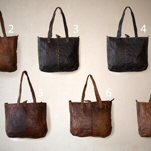 Puede incluir: Colecci&oacute;n de bolsos tote de cuero en varios tonos de marr&oacute;n y negro. Cada bolso tiene forma rectangular, asas largas y una superficie texturizada. Los bolsos se exhiben sobre un fondo neutro, mostrando su dise&ntilde;o r&uacute;stico y duradero.