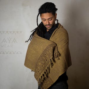 May include: A person wearing a brown shawl with a geometric pattern and fringe. The shawl is wrapped around the person's shoulders and neck. The person has long, dark hair and is looking down.
