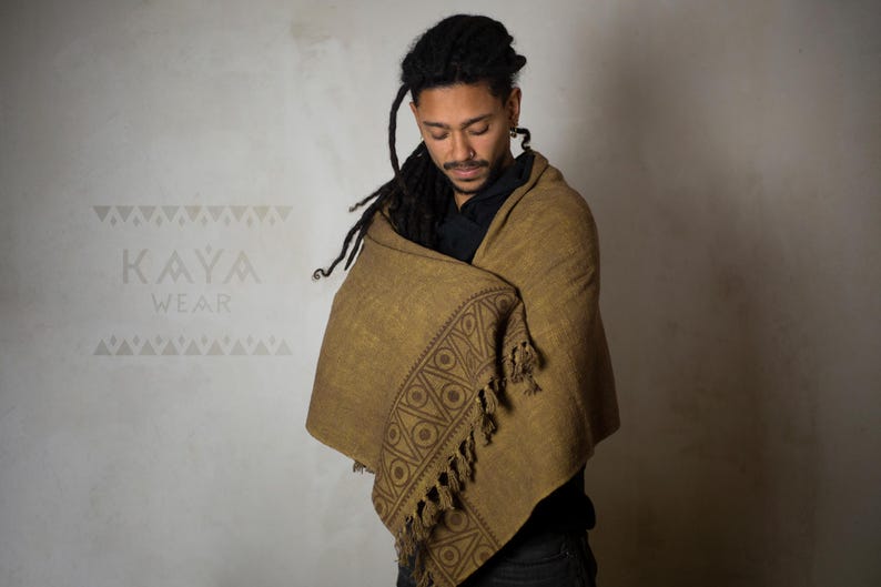 May include: A person wearing a brown shawl with a geometric pattern and fringe. The shawl is wrapped around the person's shoulders and neck. The person has long, dark hair and is looking down.