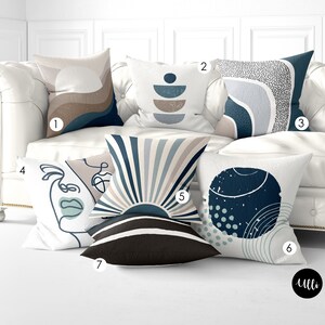 May include: Six decorative throw pillows with abstract geometric designs in shades of blue, brown, and white. The pillows are arranged on a white couch.