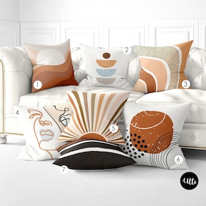 May include: Six different throw pillows with abstract designs in shades of brown, orange, white, and black. The pillows are arranged on a white couch.
