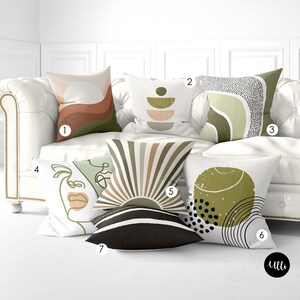 May include: A white couch with six throw pillows featuring abstract geometric designs in shades of green, brown, and beige. The pillows have different patterns, including stripes, circles, and lines.