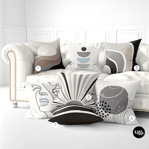 May include: Six decorative throw pillows with abstract geometric designs in black, white, gray, and blue. The pillows are arranged on a white couch.
