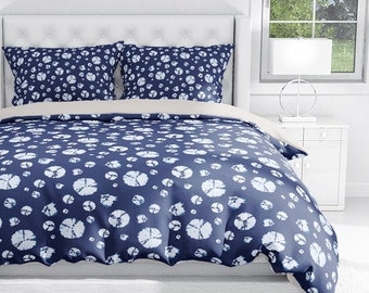 May include: A navy blue duvet cover with a white pattern of circles. The duvet cover is on a bed with white sheets and two matching pillowcases. The bed is in a white room with two windows and a white lamp on each side of the bed.
