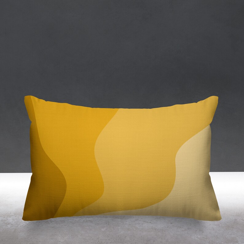Puede incluir: Una almohada rectangular con un patr&oacute;n abstracto amarillo y beige. La almohada tiene una tela suave y texturizada.