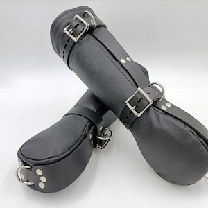 May include: A pair of black leather restraints with silver buckles and rings. The restraints are designed to be worn on the wrists.