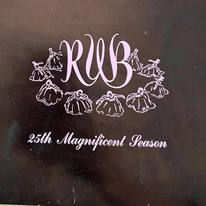 May include: A black program cover with the text "RWB" in a stylized font, surrounded by illustrations of dancers. The text "25th Magnificent Season" is below the illustrations. The cover is slightly worn.