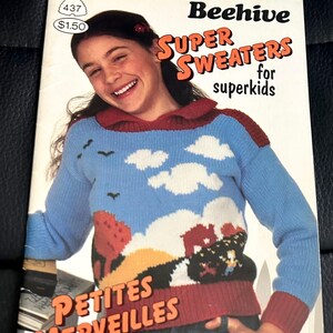 May include: A vintage book cover titled "Beehive Super Sweaters for Superkids" featuring a girl wearing a blue sweater with a landscape design. The sweater has a red collar and cuffs. The cover also includes the text "Petites Merveilles pour enfants".