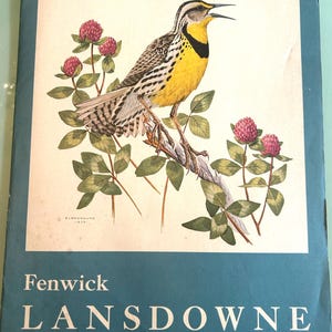 Puede incluir: Una portada de libro vintage con una ilustración detallada de un pájaro amarillo y negro posado en una rama con flores rosas y hojas verdes. El texto "Fenwick Lansdowne" está impreso en blanco sobre un fondo verde azulado.