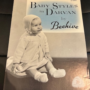 May include: A vintage baby clothing pattern book titled "Baby Styles in Darvan by Beehive." The cover shows a black and white photo of a baby in a knitted bonnet, cardigan, dress, and booties. The price is 35 cents.