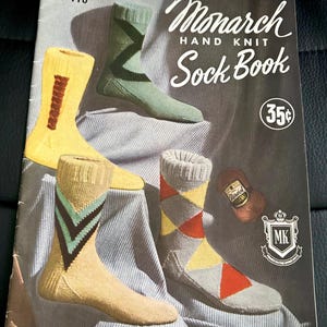 May include: A vintage "Monarch Hand Knit Sock Book" cover showing four pairs of knitted socks in various colours and patterns. The socks feature stripes and argyle designs. The cover also includes the price, "35¢", and the text "FOR NUMBERS AND KNITTING INSTRUCTIONS SEE CHART ON PAGE 4."