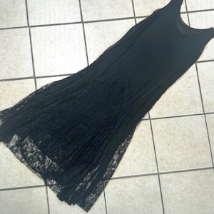 Könnte beinhalten: Ein ärmelloses schwarzes Kleid mit Rundhalsausschnitt und einem figurbetonten Oberteil, das in einen ausgestellten Rock übergeht. Der untere Teil des Rocks besteht aus transparentem, filigranem schwarzem Spitzenstoff mit Blumenmuster und gewelltem Saum.