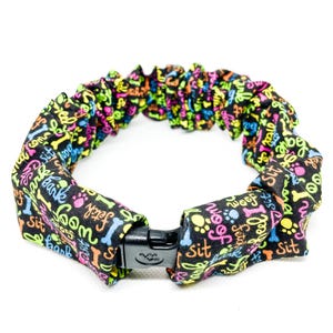 May include: A black, elastic dog collar with a colorful print of dog-related words and paw prints. The collar has a black plastic buckle.