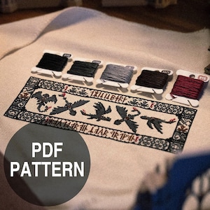 Puede incluir: Un patrón PDF de punto de cruz con un diseño de dragón, bordado con hilo negro, gris y rojo. El patrón está sobre tela beige, con carretes de hilo en varios tonos de gris, negro y rojo. El texto "PDF PATTERN" es visible.