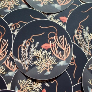 Op de afbeelding: Een set ronde stickers met een donkerblauwe achtergrond waarop koralen, zeewier en kleine oranje vissen zijn afgebeeld. De stickers zijn perfect om een ​​toets van zeeleven aan je spullen toe te voegen.