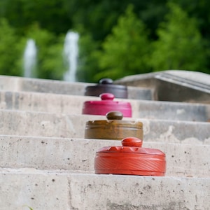 Peut inclure: Quatre boîtes en bois avec couvercles, empilées sur des marches en béton. Les boîtes sont peintes dans différentes couleurs : brun foncé, rose, brun et rouge.