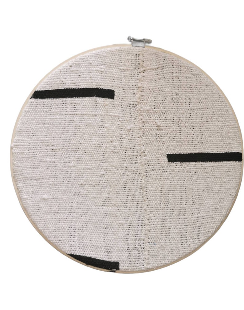 May include: A white circular embroidery hoop with black lines painted across the fabric.