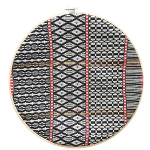 May include: A round, black and white patterned fabric stretched over a wooden embroidery hoop. The fabric has a geometric design with red and yellow accents.