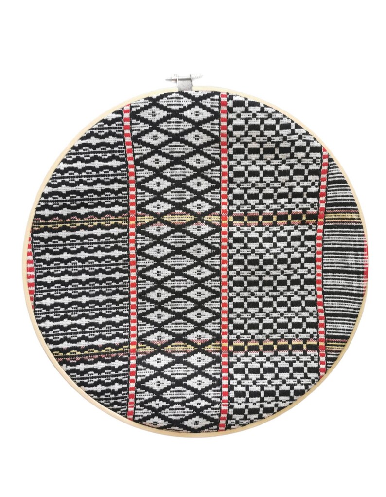 May include: A round, black and white patterned fabric stretched over a wooden embroidery hoop. The fabric has a geometric design with red and yellow accents.
