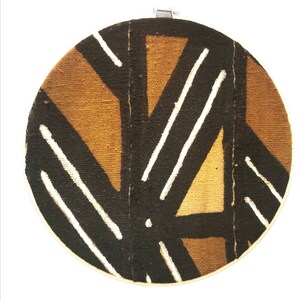 May include: A round wall hanging with a geometric pattern in brown, white, and black. The pattern is made of stripes and triangles.