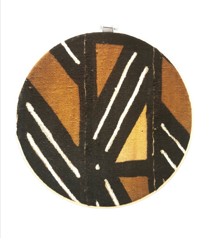 May include: A round wall hanging with a geometric pattern in brown, white, and black. The pattern is made of stripes and triangles.
