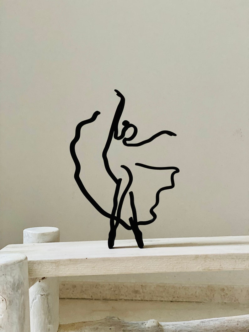 May include: Black metal sculpture of a ballerina in a flowing skirt pose.