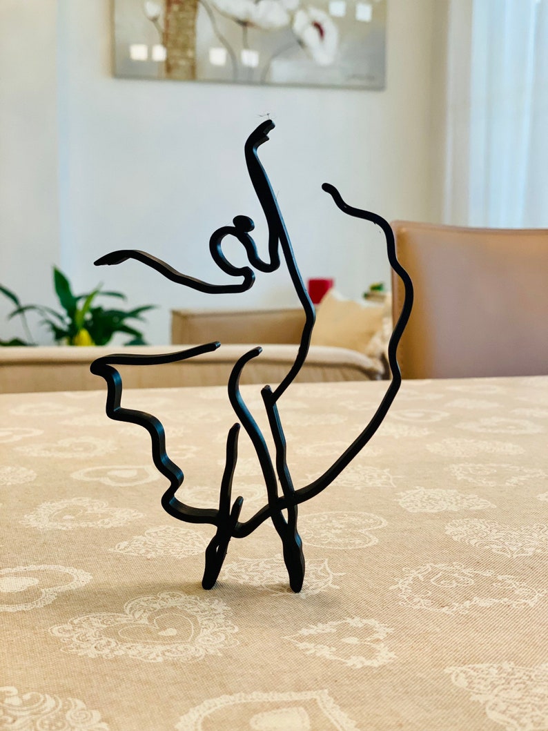 May include: A black metal sculpture of a ballerina in a graceful pose. The sculpture is made of thin wire and has a delicate, minimalist design.