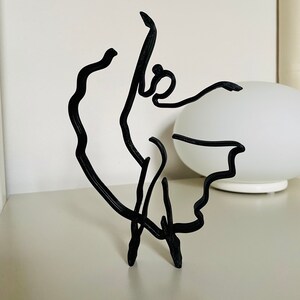 May include: Black wire sculpture of a ballerina in a flowing pose.