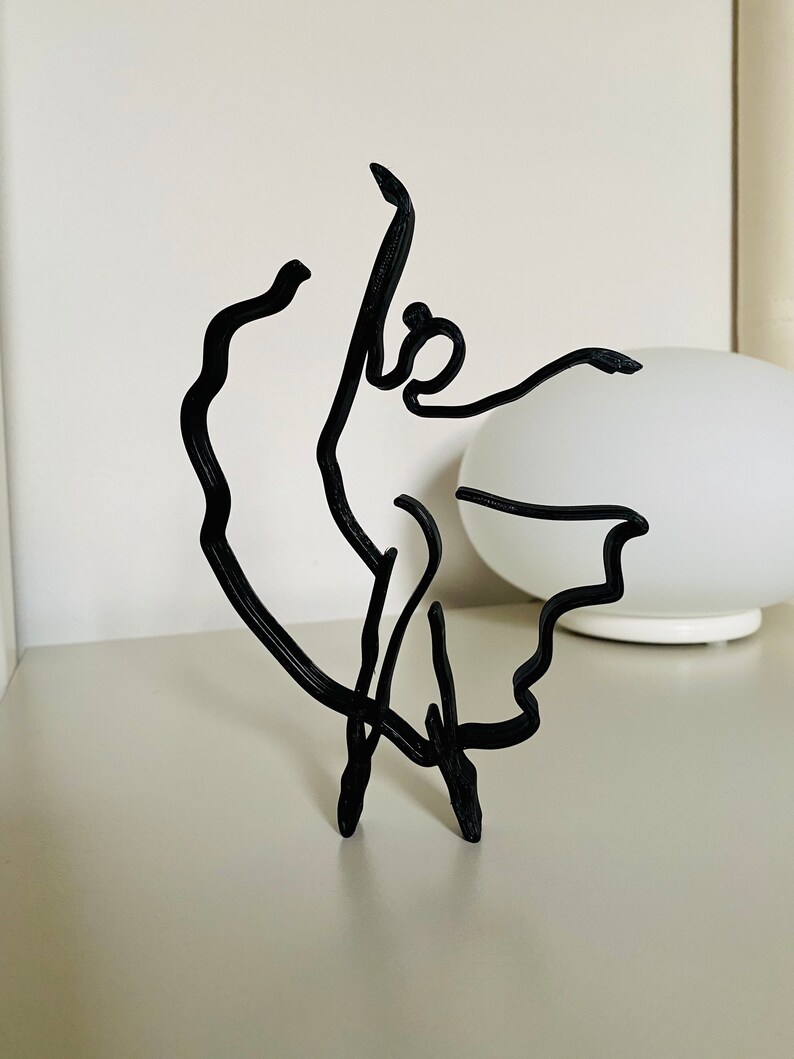 May include: Black wire sculpture of a ballerina in a flowing pose.