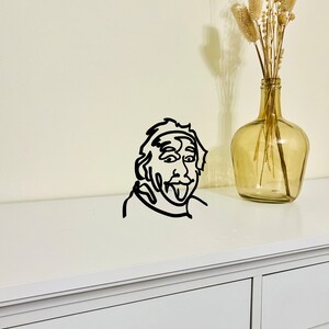 Puede incluir: Decoraci&oacute;n de pared de arte de l&iacute;nea en blanco y negro de una persona sacando la lengua. El arte est&aacute; montado en una c&oacute;moda blanca con un caj&oacute;n.