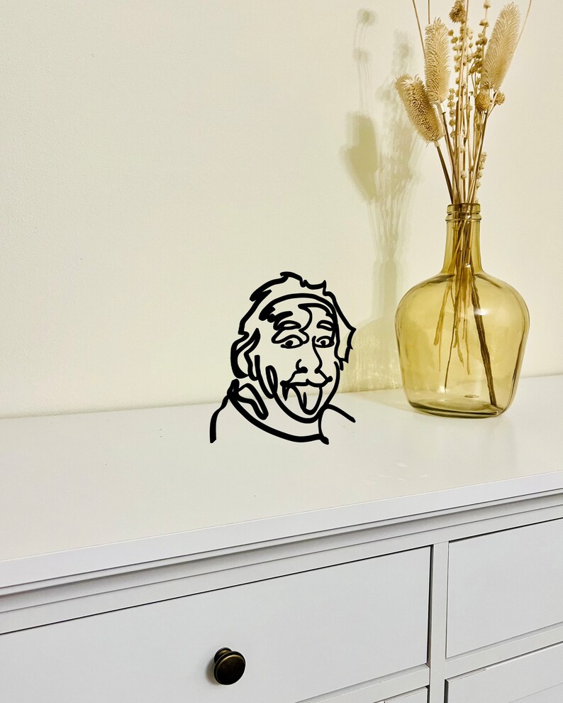 Puede incluir: Decoraci&oacute;n de pared de arte de l&iacute;nea en blanco y negro de una persona sacando la lengua. El arte est&aacute; montado en una c&oacute;moda blanca con un caj&oacute;n.