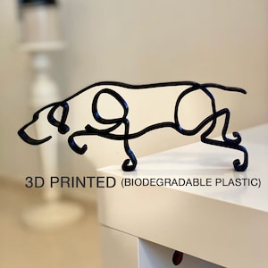 Puede incluir: Una escultura de perro negra impresa en 3D, hecha de plástico biodegradable. La escultura es de estilo minimalista, con un diseño simple de líneas.