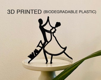 May include: A 3D printed black plastic figurine of a couple dancing. The figurine is on a white pedestal and the word "Waltz" is printed on the base. The figurine is made from biodegradable plastic.