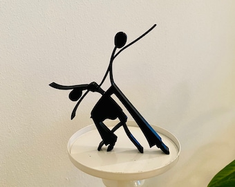 May include: A black metal sculpture of two figures dancing. The sculpture is on a white pedestal.