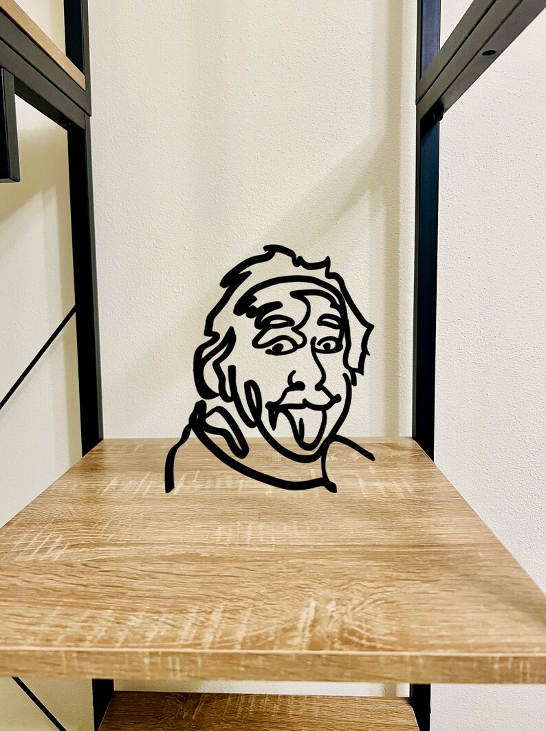 Puede incluir: Escultura de pared de metal negro de un rostro con la lengua fuera. La escultura est&aacute; en un estante de madera.